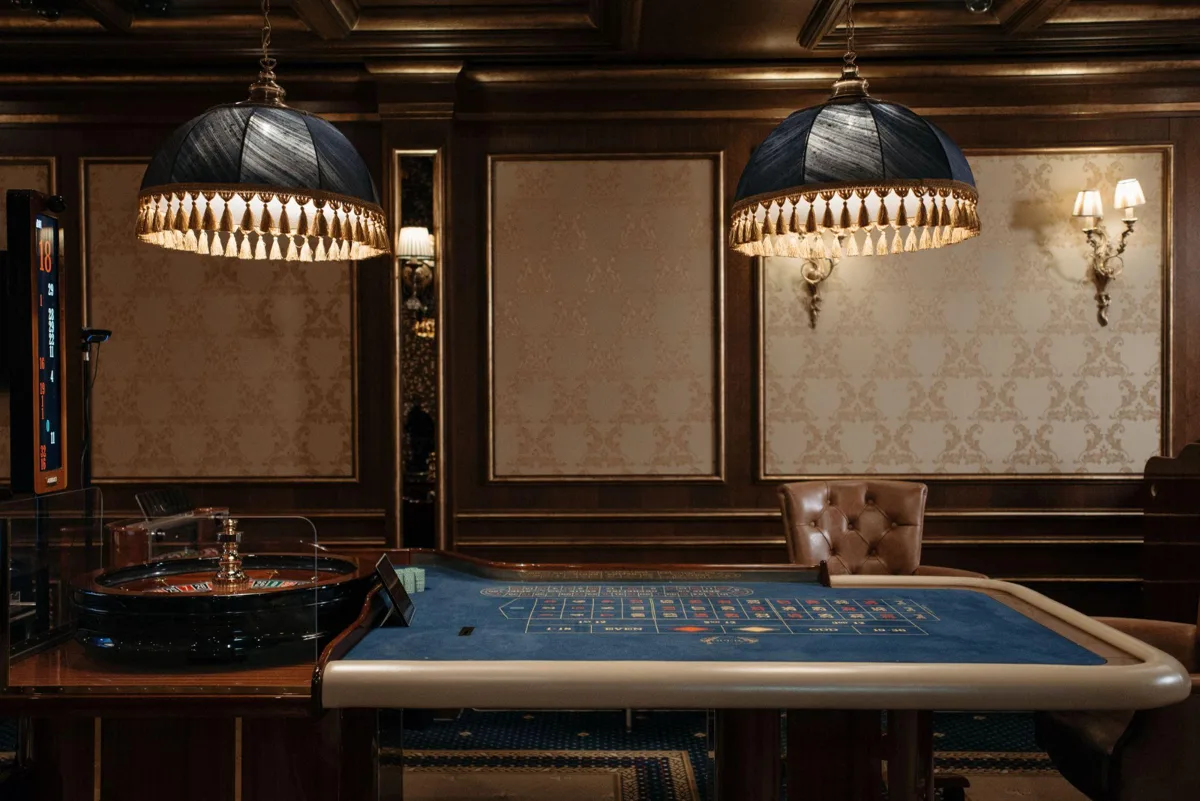 Klassisk casinosalong med rouletthjul och blått spelbord under två lampor med tofsar
